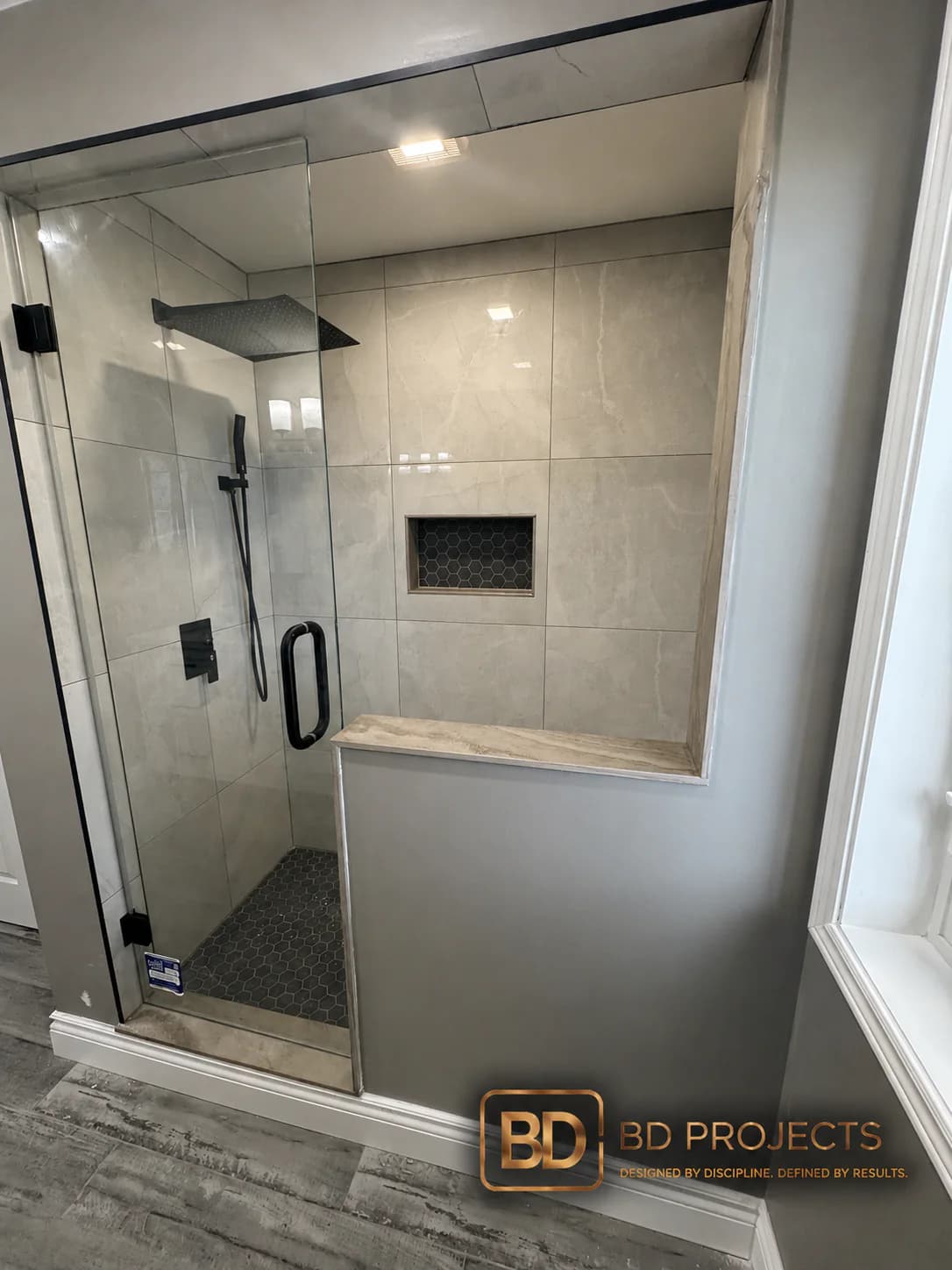 Completed glass-enclosed tile shower with black fixtures and a built-in niche